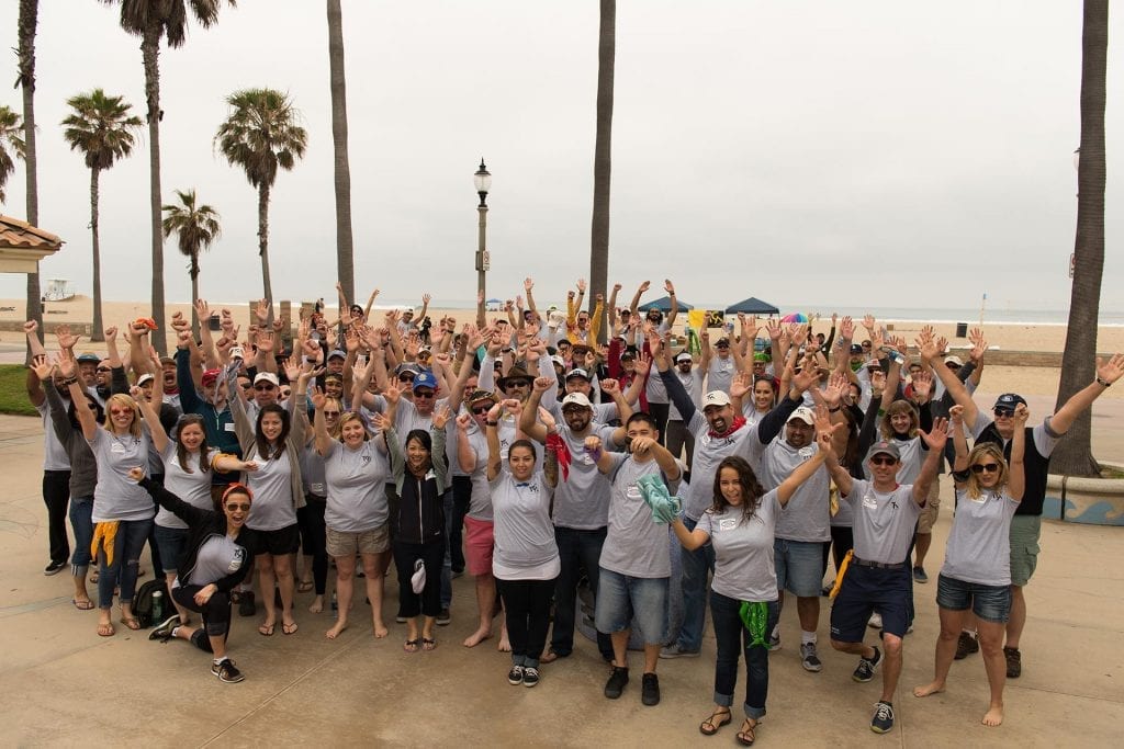 A large group of participants celebrates after completing a beachside team building event.