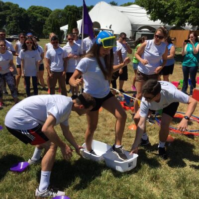 Participants in white shirts engage in a fun and wacky relay challenge during an Outrageous Games team building event, with one person wearing a snorkel mask.