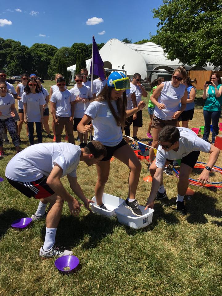 Participants in white shirts engage in a fun and wacky relay challenge during an Outrageous Games team building event, with one person wearing a snorkel mask.