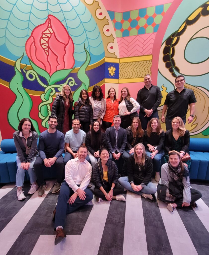 Team photo in front of a vibrant mural during a Mystery Bus team building event, capturing a moment of camaraderie and excitement.