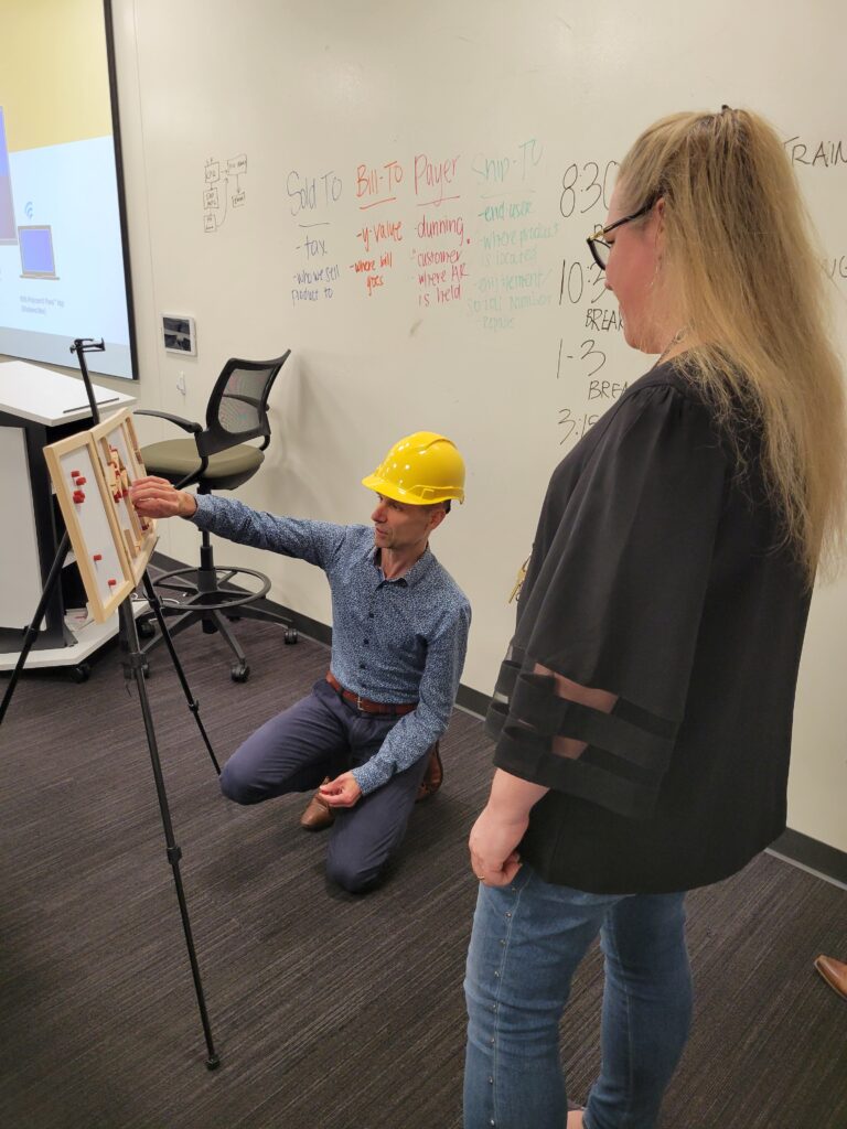 Team building activity focused on communication and problem-solving. A participant wearing a hard hat carefully assembles a model while receiving guidance, emphasizing teamwork, strategy, and clear instructions.