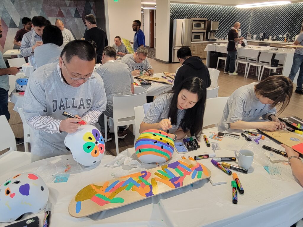 Participants are busy decorating helmets and skateboards during a CSR team building event. The table is filled with various markers and materials as individuals focus on creating colorful and unique designs.