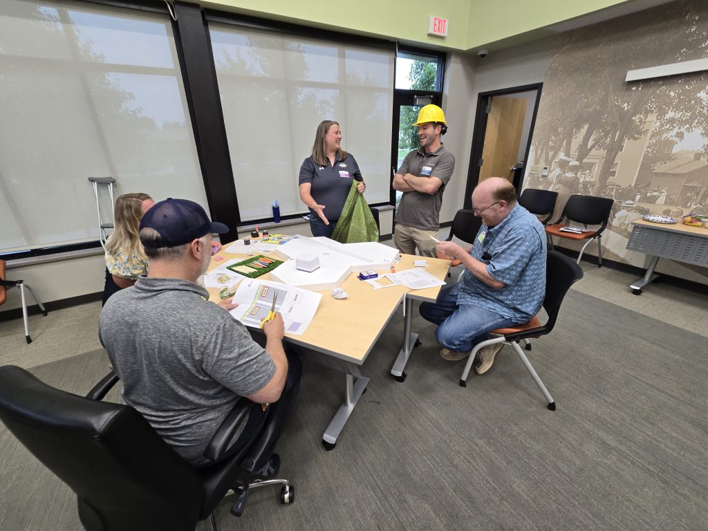 Team members collaborating at a table during the City Build team building event, planning their miniature city model with materials and blueprints.