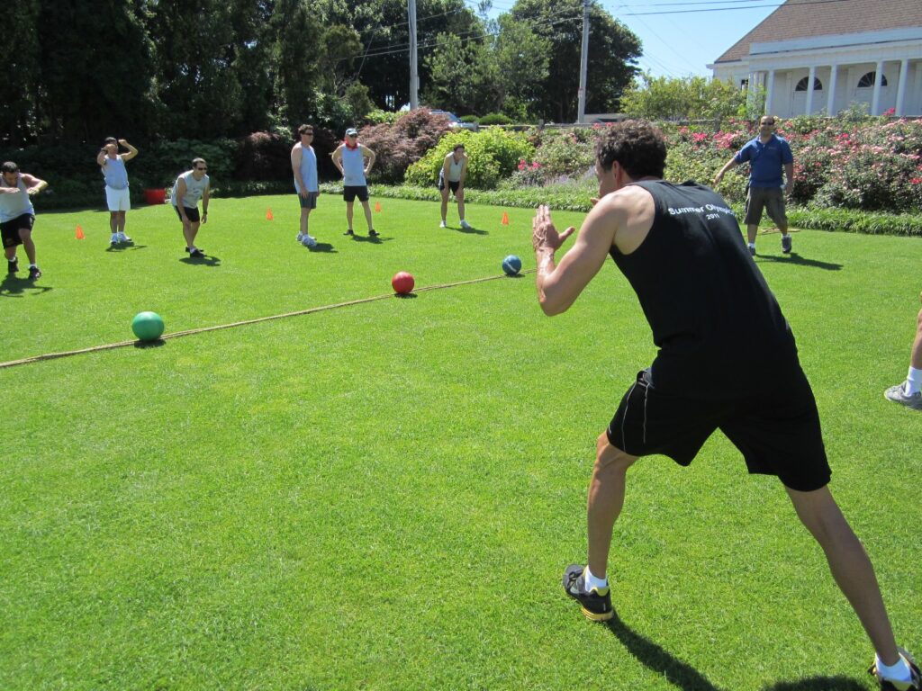 Participants gearing up for a dodgeball challenge during the Outrageous Games team building event on a sunny lawn.