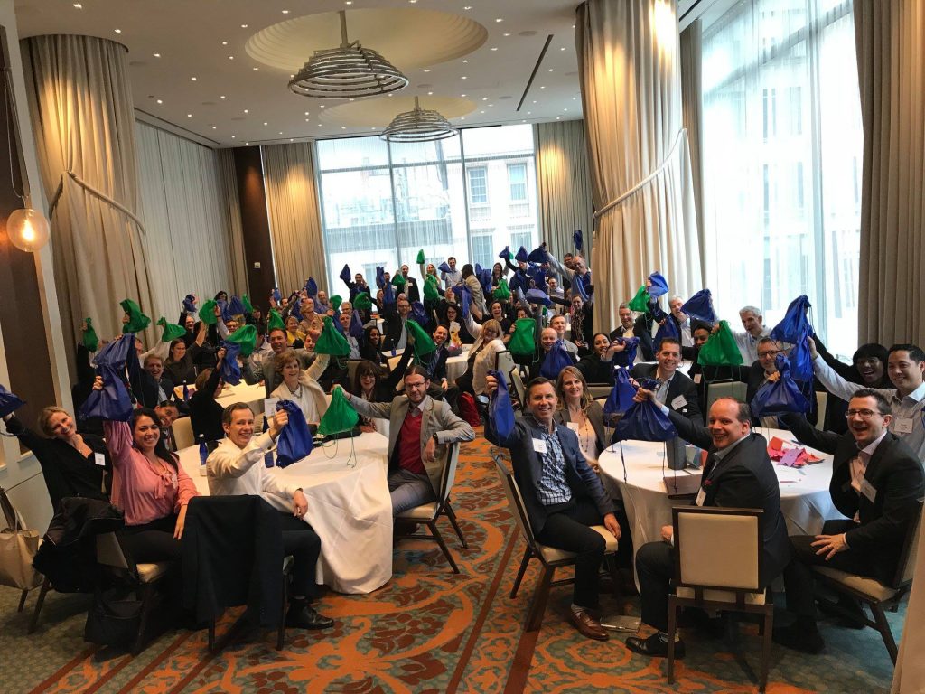 Team members posing with colorful bags during the Team Disaster Relief event. Participants work together to assemble disaster relief care kits, bonding over fun challenges that foster teamwork and communication.