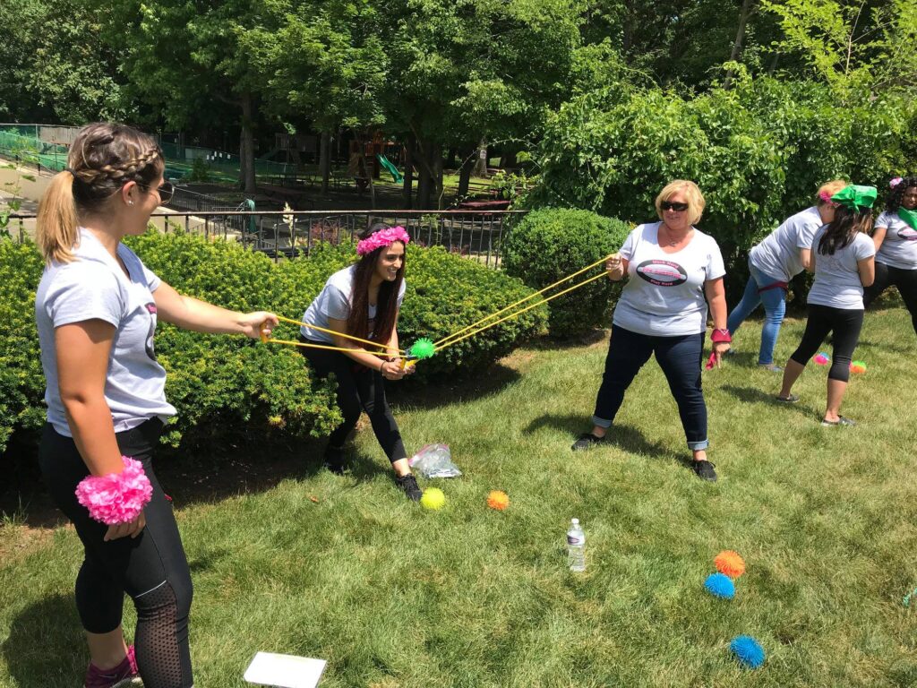 Team members participate in an outdoor team building challenge using slingshots to launch colorful objects in a playful competition.