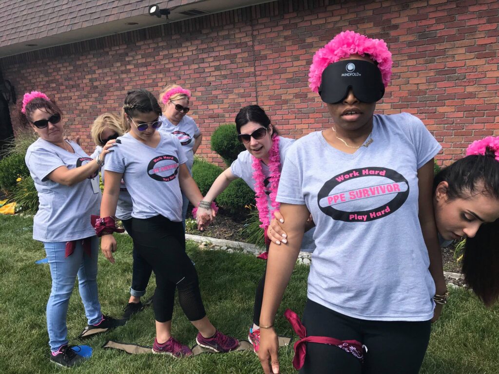 Team members navigating an outdoor challenge blindfolded during a Survivor-style team building event.