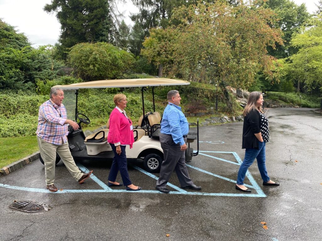 Team members recreate the iconic Abbey Road crossing in a lighthearted moment during the Healthcare Heroes team building event. Four participants walk in a line in front of a golf cart, mimicking the famous Beatles pose, bringing fun and engagement to the event which embraces Corporate Social Responsibility by supporting local healthcare professionals.