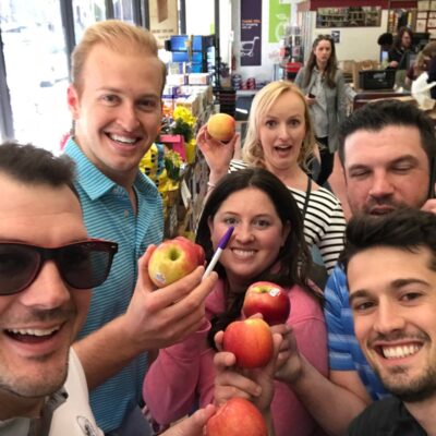 Team posing with apples inside a grocery store during a challenge for the Team-opoly scavenger hunt event.