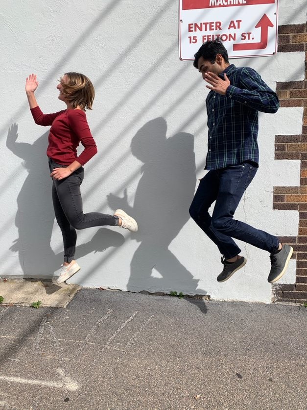 Two participants joyfully jumping in the air, creating playful shadows on a wall during the Healthcare Heroes scavenger hunt team building program.