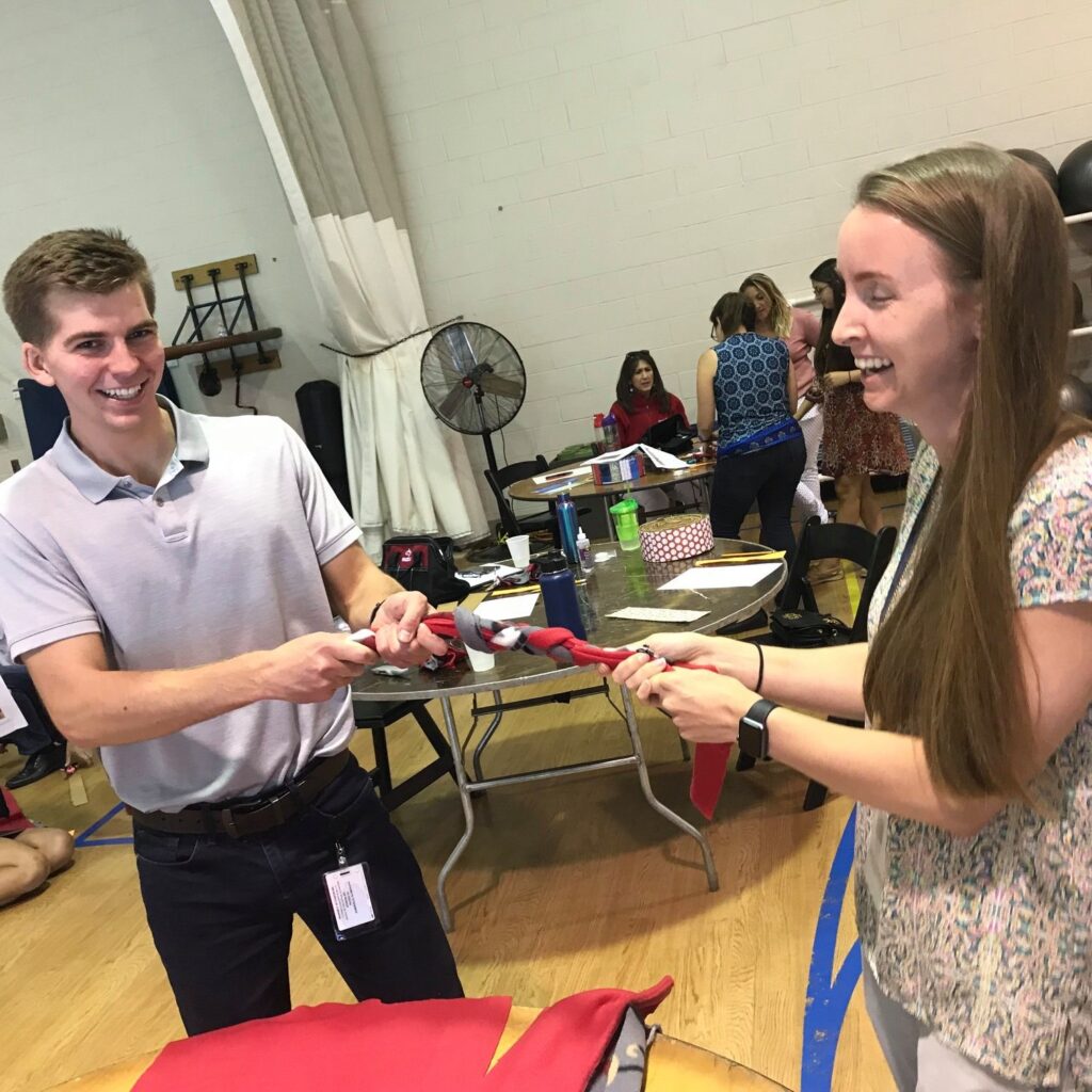 Two participants smiling and playing tug-of-war with a braided toy during the Foster Pet Care Kits activity at a corporate charitable team building event called 'the Donation Station'.