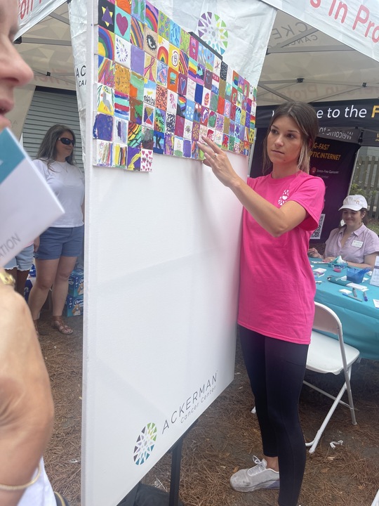 Participant placing painted mini pieces of art onto a large board to create a mural during the Make-A-Mini-Mural activity at a corporate charitable team building event called 'the Donation Station'.