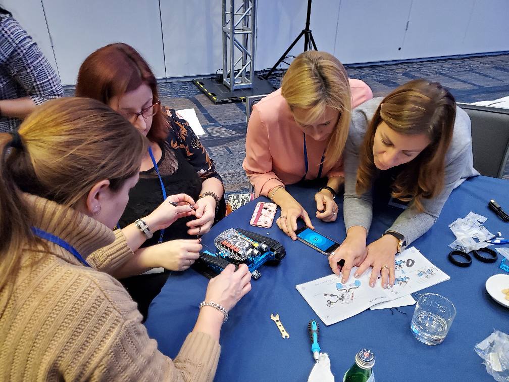 A team of four participants focuses on assembling a robot, using tools and an instruction manual as part of a team building activity. They are seated around a table, collaborating on the technical task.