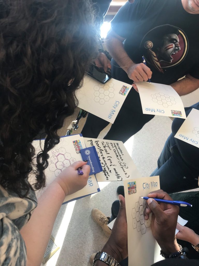 Team members collaborating on city maps at a City Build team building event, sketching ideas and planning zones for their project.