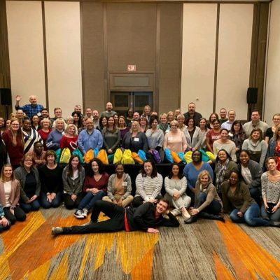 Large group gathered together for the Team Disaster Relief event, proudly holding their colorful bags. They collaborated to assemble disaster relief kits, engaging in teamwork and problem-solving challenges to support recovery efforts.