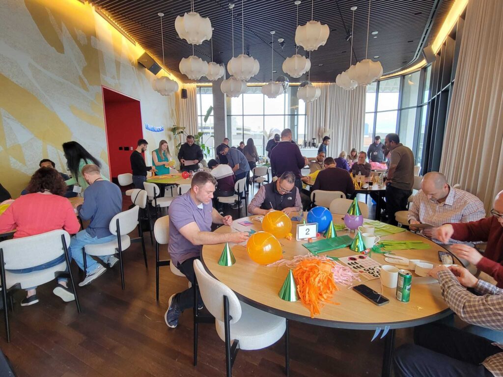 Participants seated at tables, assembling birthday kits with balloons, party hats, and decorations during at a corporate team building event, called 'The Donation Station'.