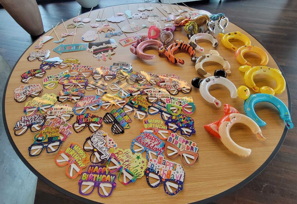 Table filled with colorful birthday-themed props, glasses, and headbands for the Birthday Kits activity at a corporate team building event, called 'The Donation Station'.