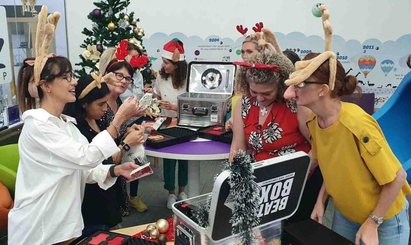 Teams dressed in festive attire work together to solve holiday-themed challenges in the Beat The Box: Rescue Santa team building event.