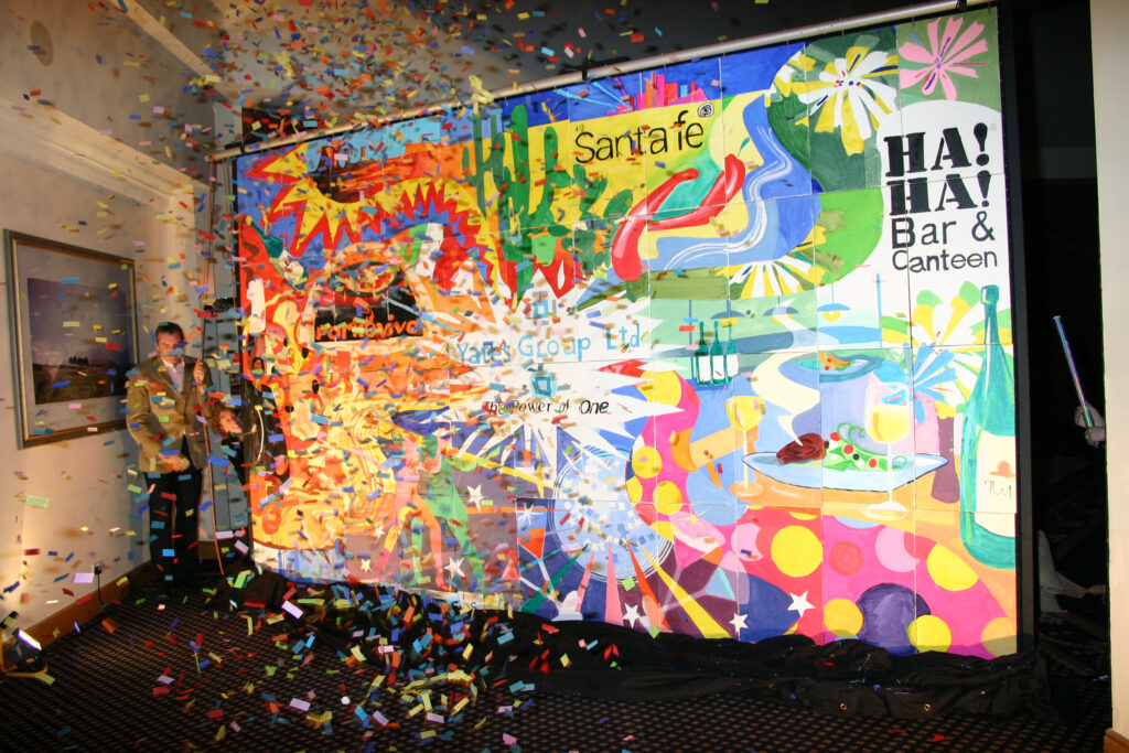 A vibrant mural is unveiled with a burst of confetti during The Big Picture team building event, celebrating collaboration and creativity.