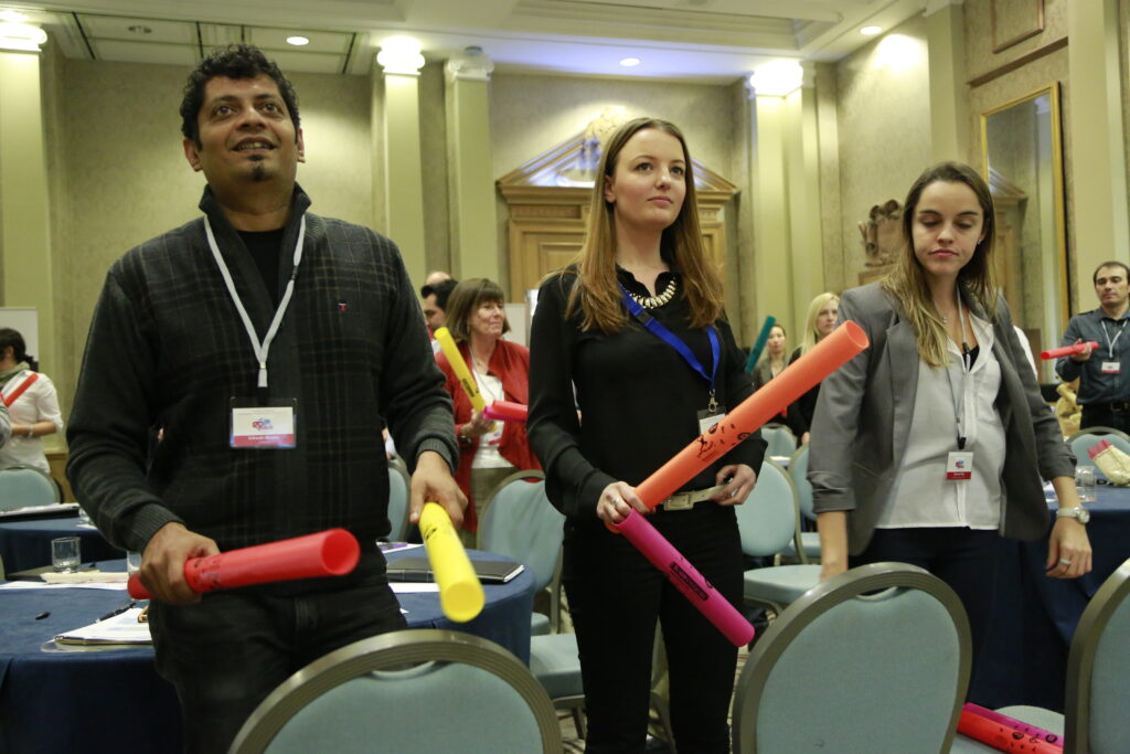 Participants standing and playing colorful Boomwhackers in sync during a musical team building activity, fostering teamwork and coordination.