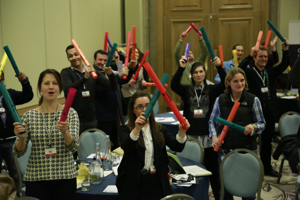 Participants enthusiastically hold colorful Boomwhackers during a high-energy Boom Time team building activity, fostering teamwork and rhythm-based collaboration.