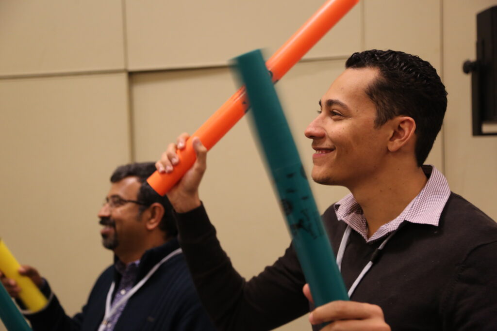 Two participants smiling and playing colorful Boomwhackers during a fun, music-based team building activity, enhancing teamwork and rhythm skills.