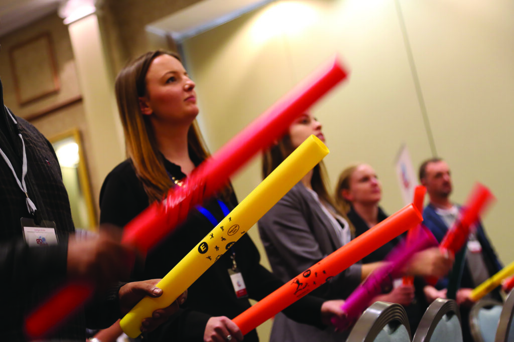 Participants engage in a Boom Time team building activity, holding colorful Boomwhackers as they follow the rhythm of the music. Focused and synchronized, they work together to create an energetic and unified musical performance.