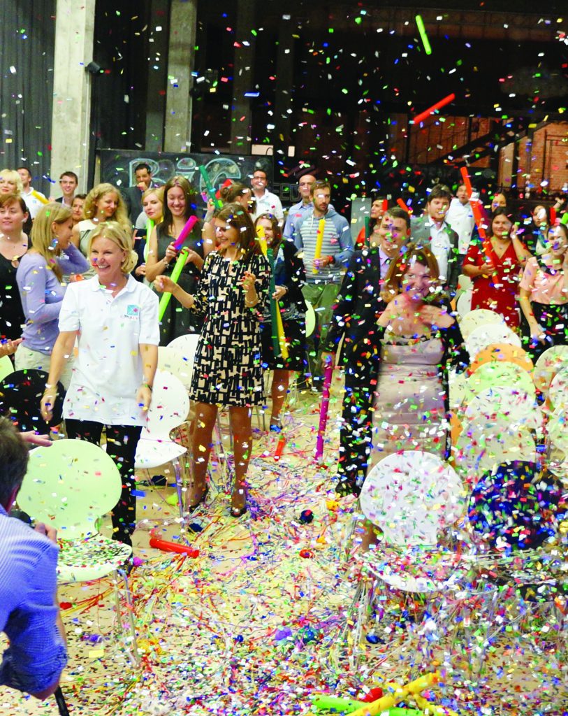 Team participating in Boom Time, a musical team building activity. Participants are surrounded by confetti and colorful Boomwhackers, collaborating to create music and enhance teamwork, energy, and communication.