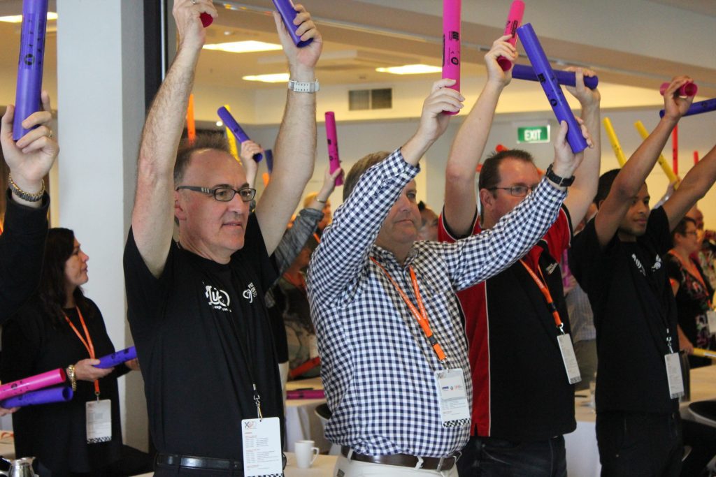 Team members participating in Boom Time, raising their Boomwhackers to play music together. This team building activity encourages collaboration, rhythm, and teamwork, creating an engaging and energetic atmosphere.