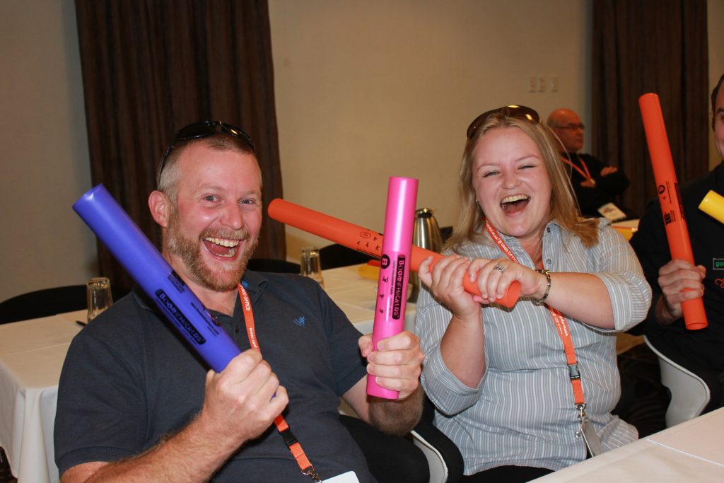 Team members smiling and laughing while participating in Boom Time, a musical team building activity. They use colorful Boomwhackers to create music, enhancing collaboration and boosting team spirit.