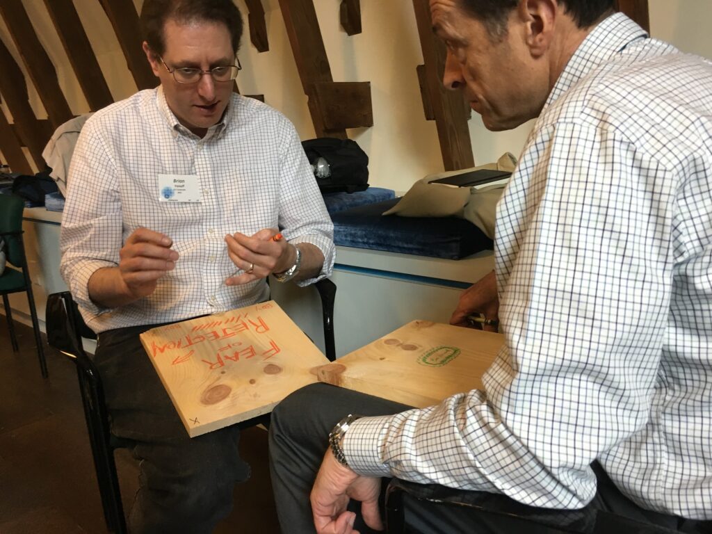 Two participants engage in a reflective moment, writing on wooden boards during a board-breaking team building event aimed at overcoming personal and professional barriers.