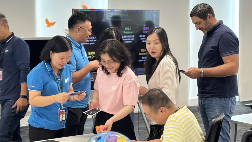 This image captures a collaborative moment during a team building event, where participants engage in an AI-powered news broadcast challenge, utilizing various roles and teamwork to create a compelling broadcast.