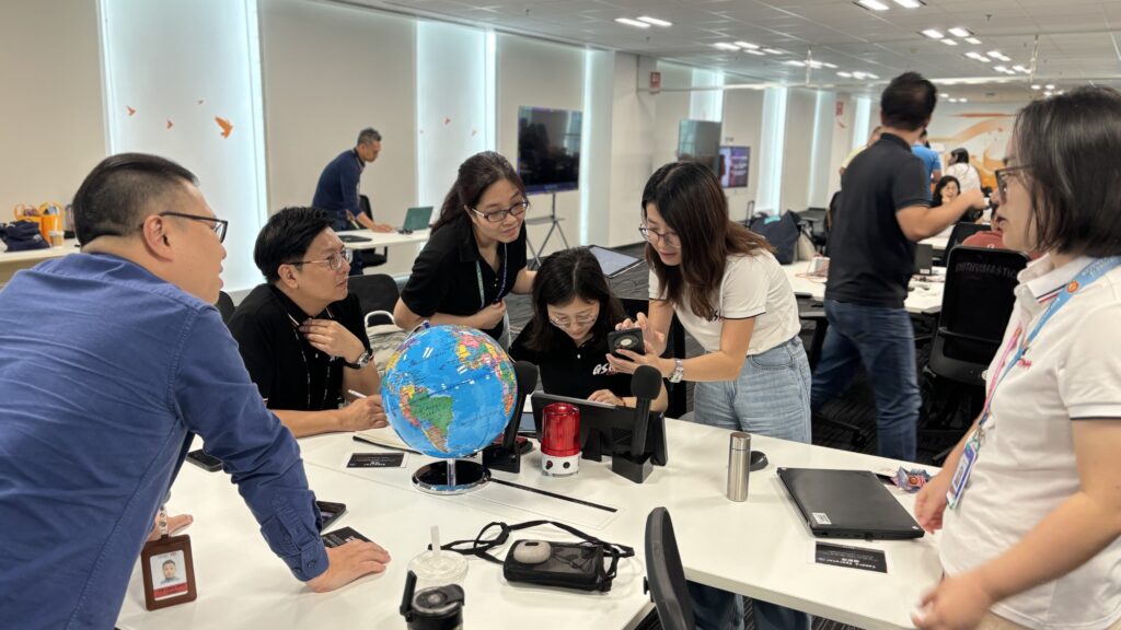 A team collaborates in a team building AI-powered news broadcast challenge, brainstorming and working together on roles like scriptwriting, research, and production.