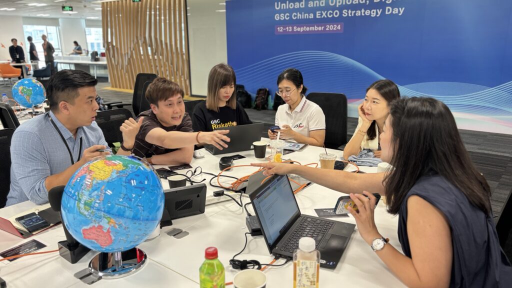 This image shows a group collaborating in a team building event, where participants are discussing strategies and working together to create a news broadcast, integrating both technology and teamwork.