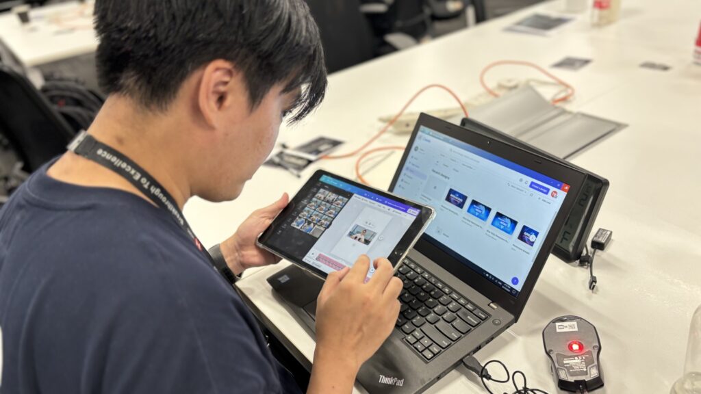 In this image, a participant is seen working with both a tablet and a laptop during a team building event. They're likely collaborating on creating a digital design or news broadcast as part of the AI-assisted project.