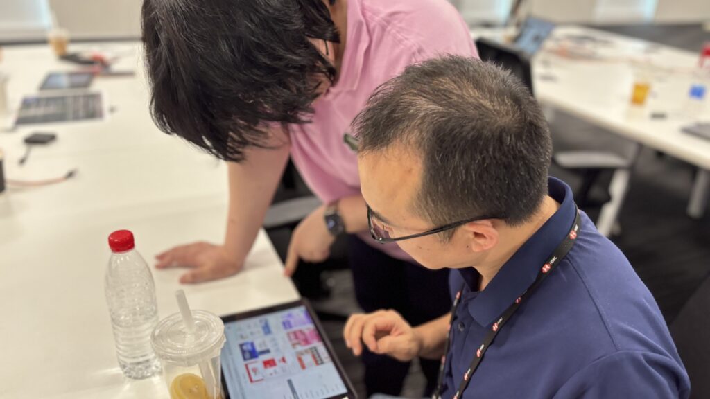 In this photo, two participants are collaborating on an iPad during a team building event focused on creating a news broadcast using AI tools. They're likely brainstorming and sharing ideas to craft their final presentation.