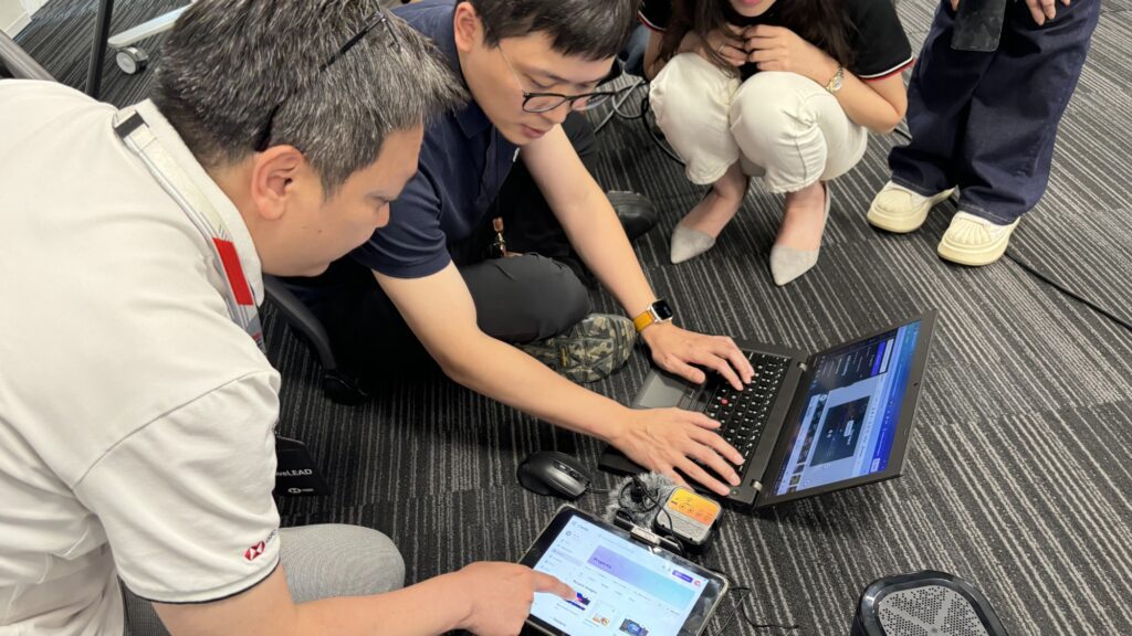 A team building activity in progress, with participants collaborating using laptops and tablets to create their AI-powered broadcasts.