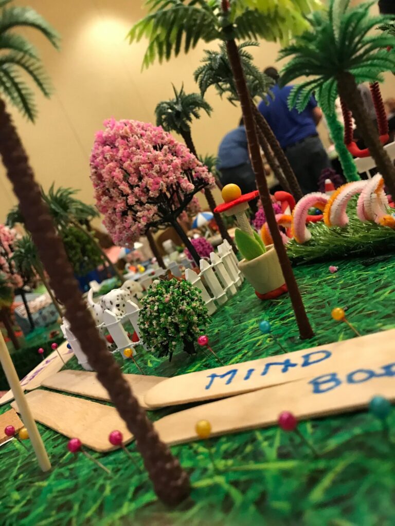 Close-up of a creative miniature city build with vibrant greenery, pink trees, and decorative pathways during a City Build team building event.