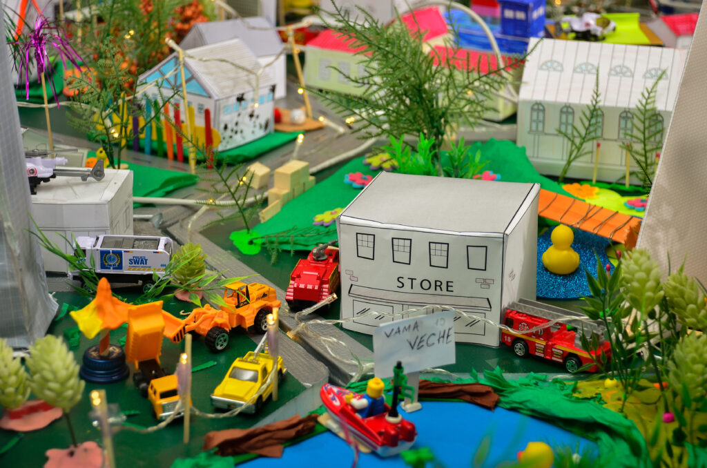 Close-up of a colorful miniature city created during the City Build team building event, featuring small buildings, toy vehicles, and greenery.