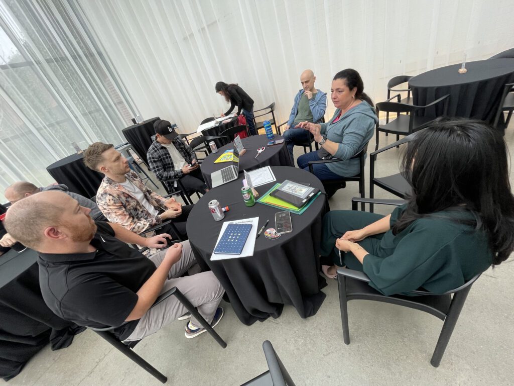 Group of team members sitting around a round table engaged in discussion on how to make a movie and what story to tell during the Corporate Film Festival team building.