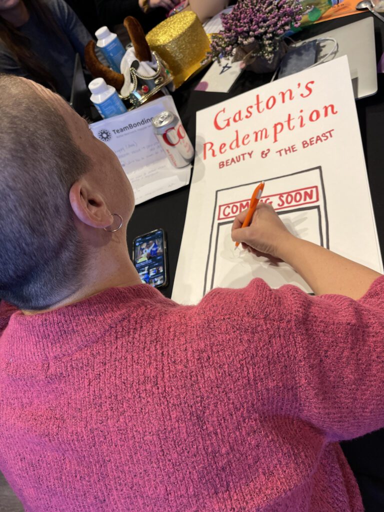 A participant draws a poster titled 'Gaston's Redemption: Beauty & The Beast' during a team building activity, showcasing creativity.