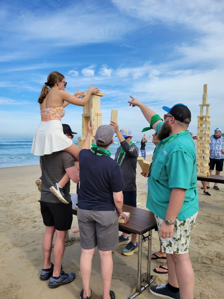 Team members work together to build a giant wooden tower on the beach during the Corporate Survivor team building event, demonstrating teamwork and communication.