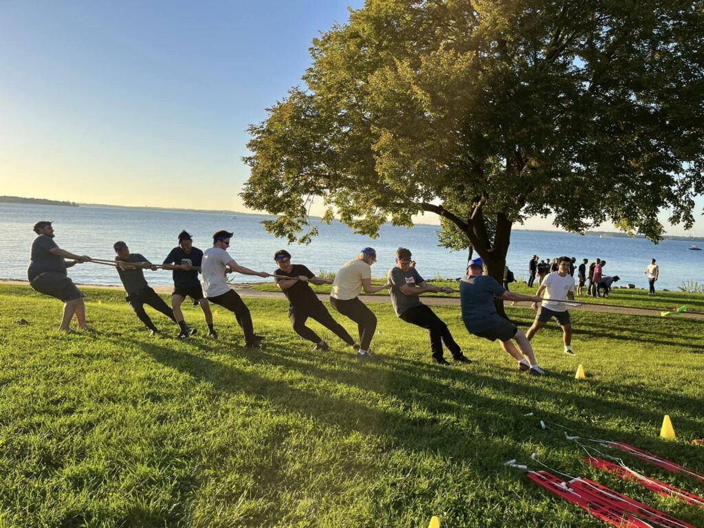 Team members engage in a tug-of-war competition by the water during a Corporate Survivor team building event, showcasing strength and collaboration.