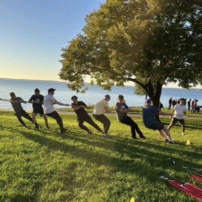 Team members engage in a tug-of-war competition by the water during a Corporate Survivor team building event, showcasing strength and collaboration.