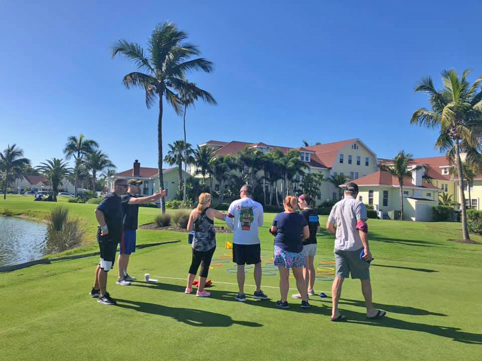 Team members gather on a golf course to strategize for a fun, outdoor team building challenge under the palm trees.