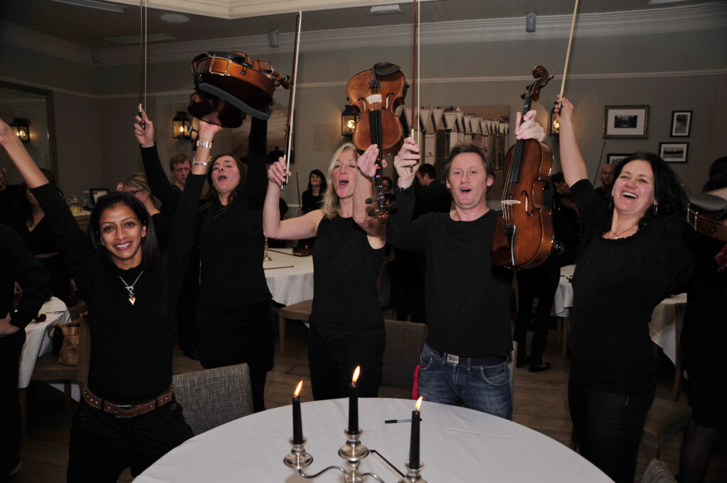 Excited participants raise their violins triumphantly after performing together during the Crescendo team building event.