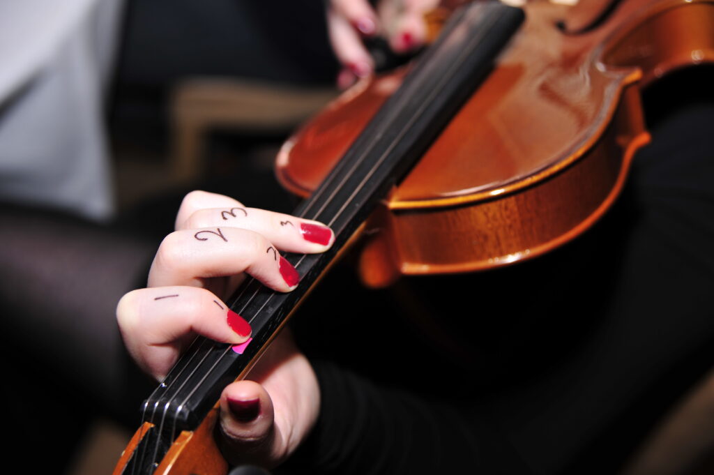 A close-up of a participant's hand learning violin finger placement during a Crescendo team building event, with numbers written on their fingers for guidance.