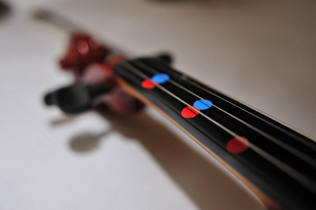 Close-up of a violin’s fingerboard with colorful markers to help participants learn notes quickly during the Crescendo team building event.