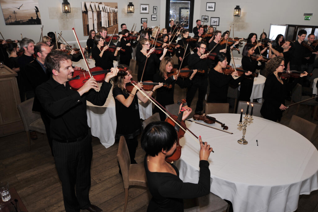 Participants perform as a unified string orchestra during the Crescendo team building event, creating harmony and teamwork through music.