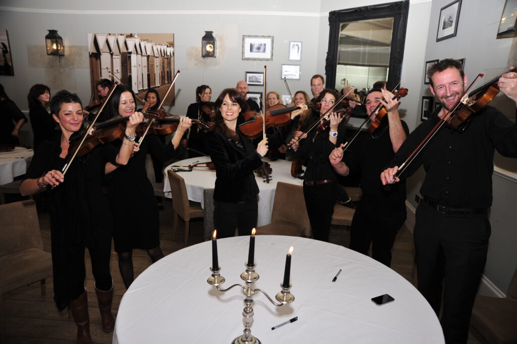 Team members confidently performing together as a string orchestra during the Crescendo team building event, showcasing collaboration and shared achievement.